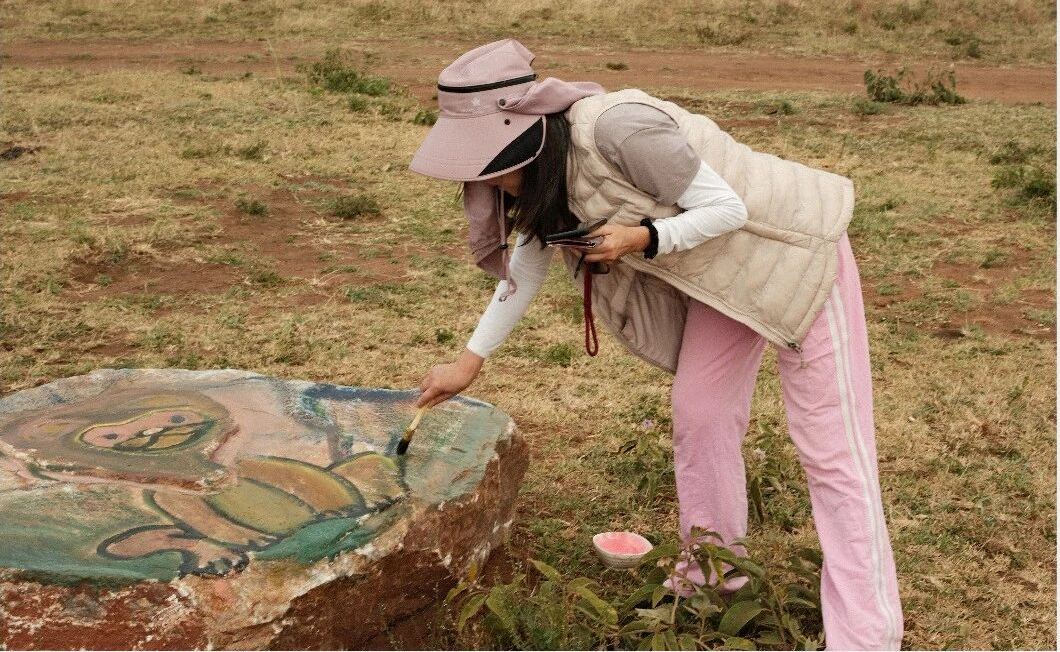 A guest painting a large rock outdoors on the grassland
