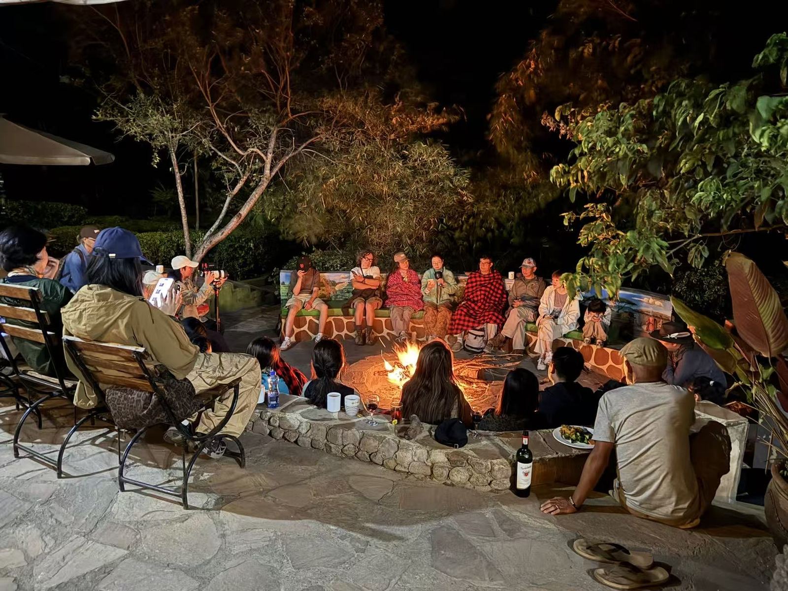 Guests seated around a fire pit on a stone terrace at night