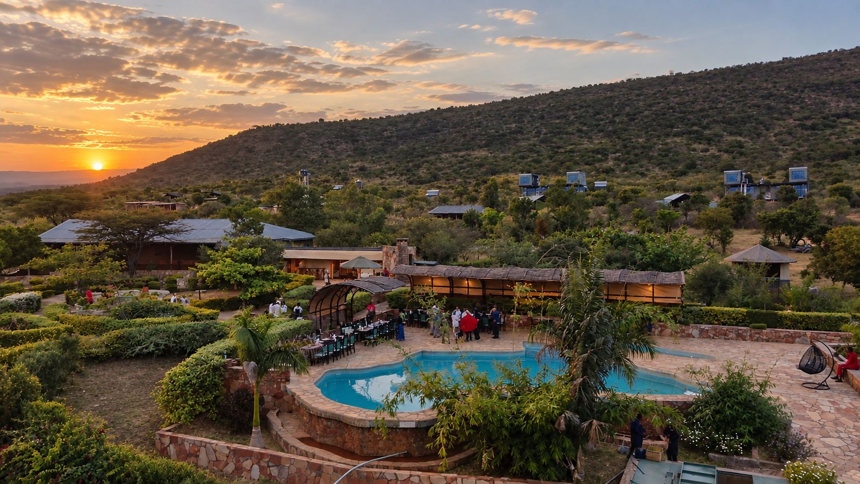 Sausage Tree seen from above at sunset: the pool and dining terrace in front, cottages among the trees and the two-storey Enkaji Villas on the hillside