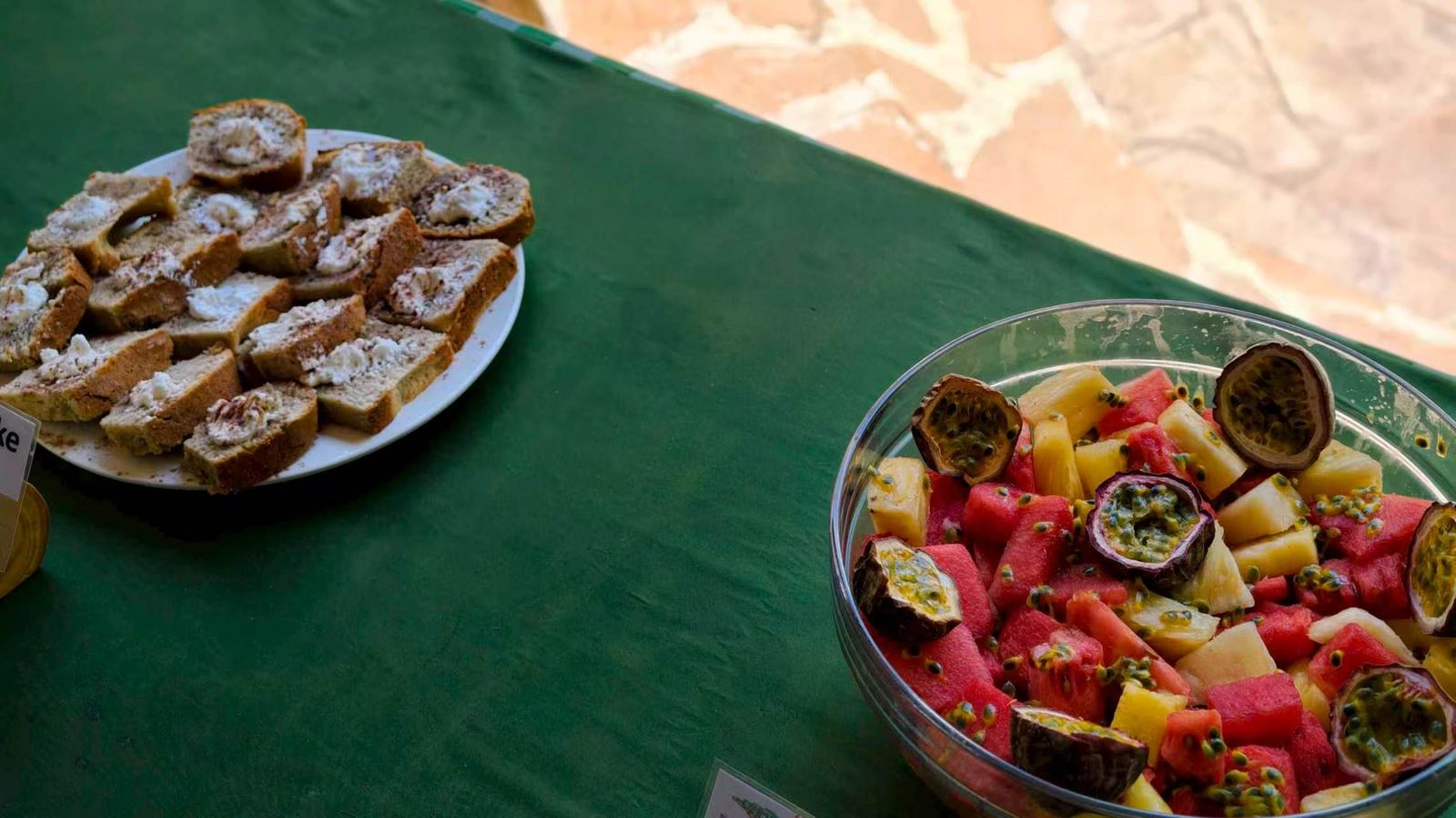 A bowl of fresh fruit salad and a plate of sliced cake on a green tablecloth