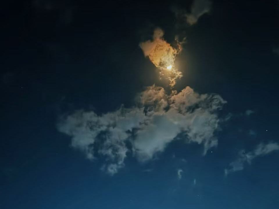 The moon breaking through clouds in a deep blue night sky over the Mara